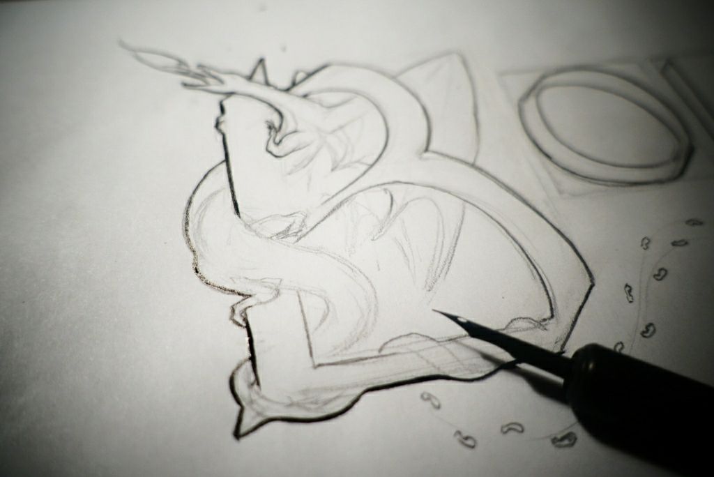 zdjęcie z procesu tworzenia okładki - stalówka na papierze, w tle smok wpisany w literę B