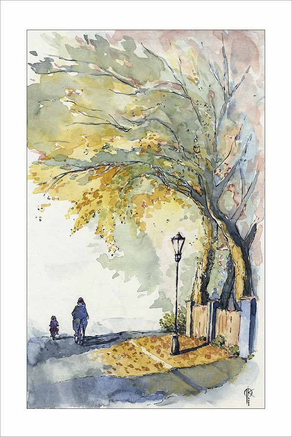 fragment uliczki i chodnika, na chodniku latarnia, w tle drzewa, ulicą jedzie dwójka rowerzystów